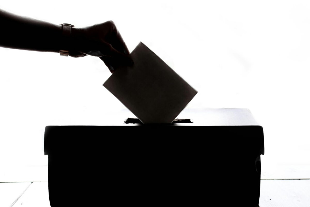 Silhouette of a hand placing a vote into a ballot box, symbolizing democracy.